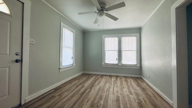 empty room with ceiling fan, crown molding, a healthy amount of sunlight, and light hardwood / wood-style flooring