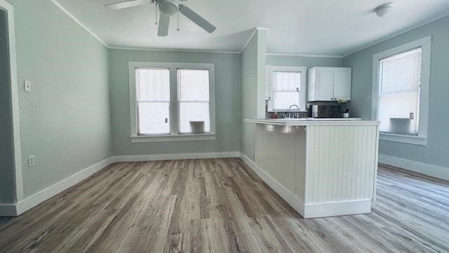 kitchen featuring white cabinetry, kitchen peninsula, ornamental molding, ceiling fan, and light hardwood / wood-style flooring