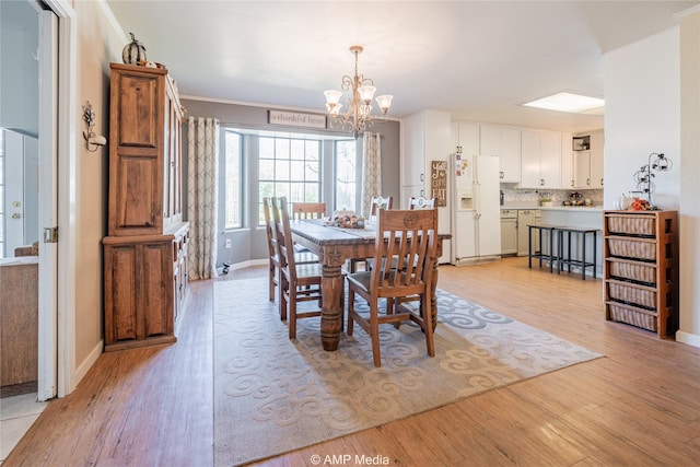 dining space with light hardwood / wood-style floors, ornamental molding, and a chandelier