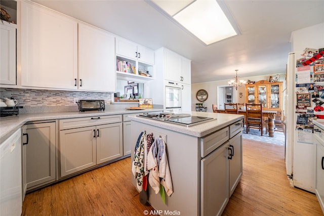 kitchen with gray cabinetry, an inviting chandelier, white appliances, decorative backsplash, and light wood-type flooring