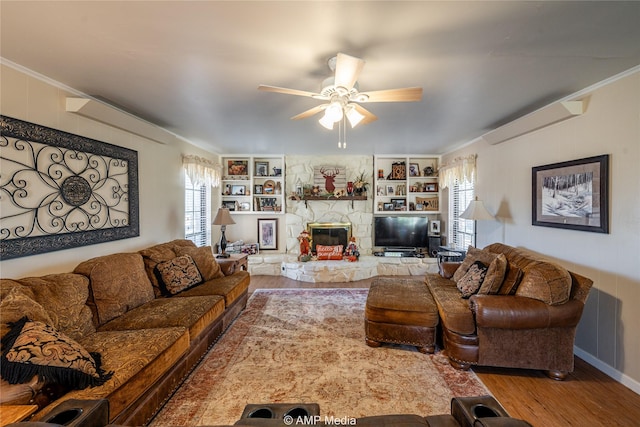 living room with hardwood / wood-style floors, crown molding, built in shelves, ceiling fan, and a fireplace