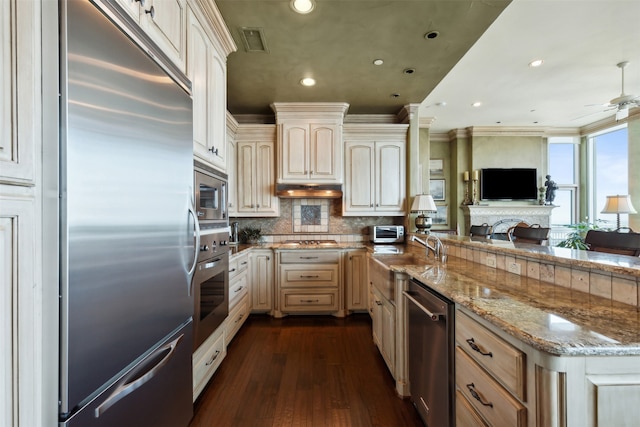 kitchen featuring light stone counters, ceiling fan, dark wood-type flooring, ornamental molding, and built in appliances