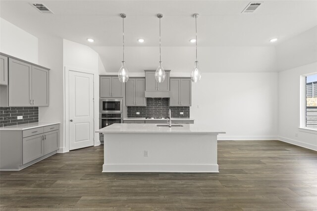 kitchen featuring pendant lighting, an island with sink, gray cabinets, and stainless steel appliances