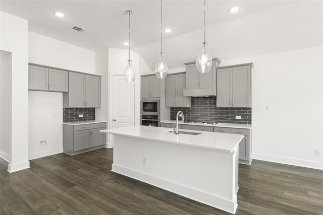 kitchen with a kitchen island with sink, gray cabinetry, lofted ceiling, dark hardwood / wood-style floors, and appliances with stainless steel finishes