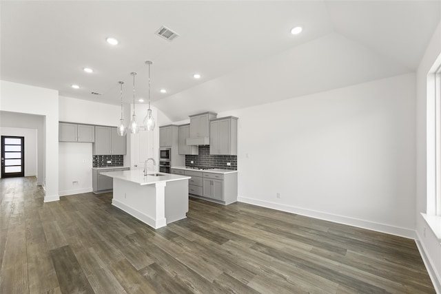 kitchen with stainless steel appliances, a center island with sink, dark wood-type flooring, and gray cabinetry