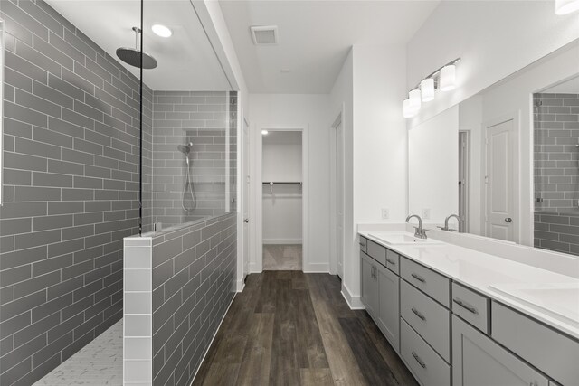 bathroom with hardwood / wood-style floors, vanity, tiled shower, and tile walls