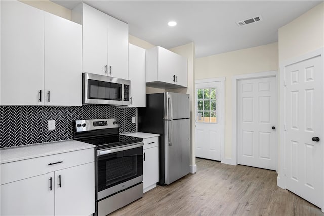 kitchen with stainless steel appliances, decorative backsplash, light wood-type flooring, and white cabinetry