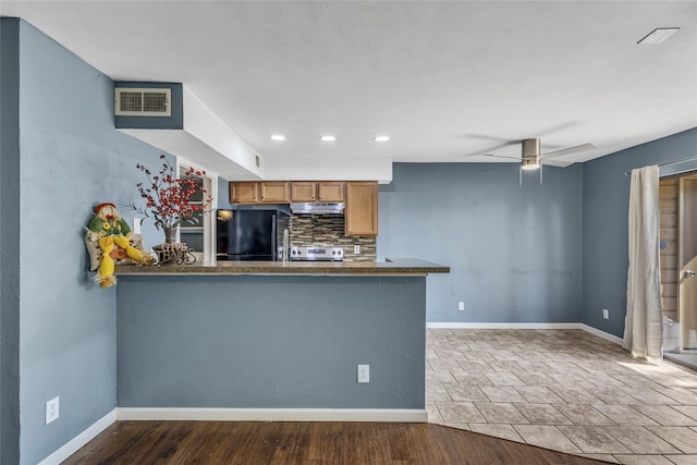 kitchen featuring decorative backsplash, black refrigerator, kitchen peninsula, and range