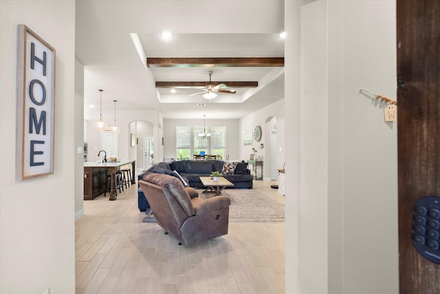 living room featuring light hardwood / wood-style flooring, beam ceiling, ceiling fan with notable chandelier, and a raised ceiling