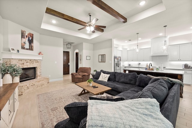 living room with ceiling fan, a tray ceiling, light wood-type flooring, and a fireplace