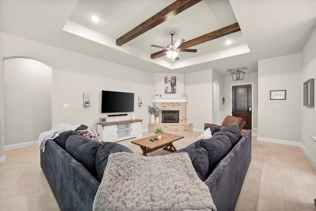 living room with a fireplace, a tray ceiling, light hardwood / wood-style floors, ceiling fan, and beamed ceiling