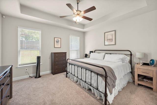 bedroom with light carpet, ceiling fan, and a raised ceiling