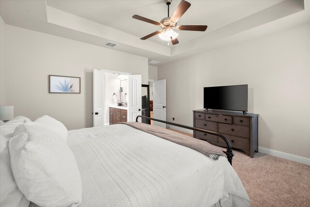 bedroom featuring a raised ceiling, ceiling fan, light colored carpet, and ensuite bath