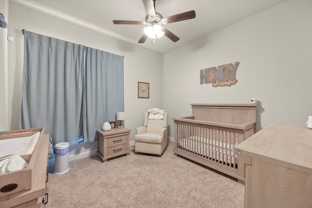 bedroom featuring light carpet, a nursery area, and ceiling fan