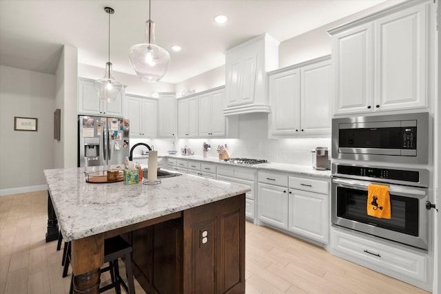 kitchen with sink, appliances with stainless steel finishes, white cabinetry, and an island with sink