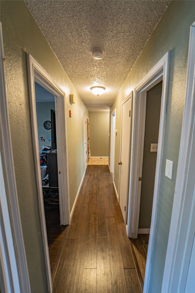 corridor with a textured ceiling and dark hardwood / wood-style flooring