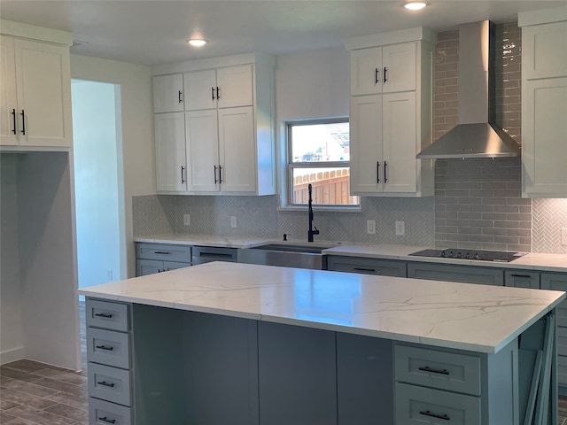 kitchen with wall chimney range hood, tasteful backsplash, a kitchen island, black electric cooktop, and white cabinets