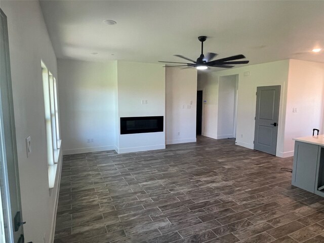 unfurnished living room featuring dark wood-type flooring and ceiling fan