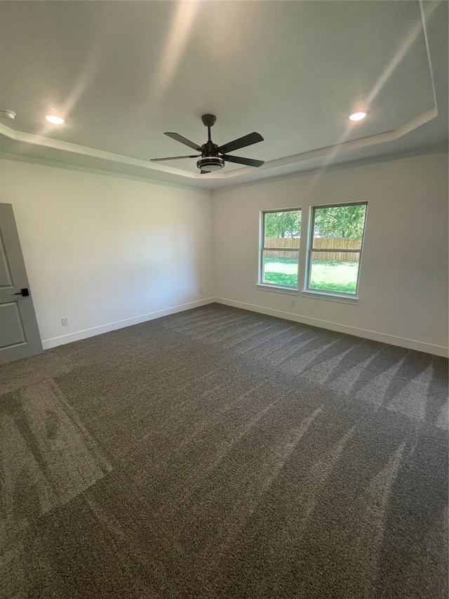 spare room featuring a tray ceiling, dark carpet, and ceiling fan