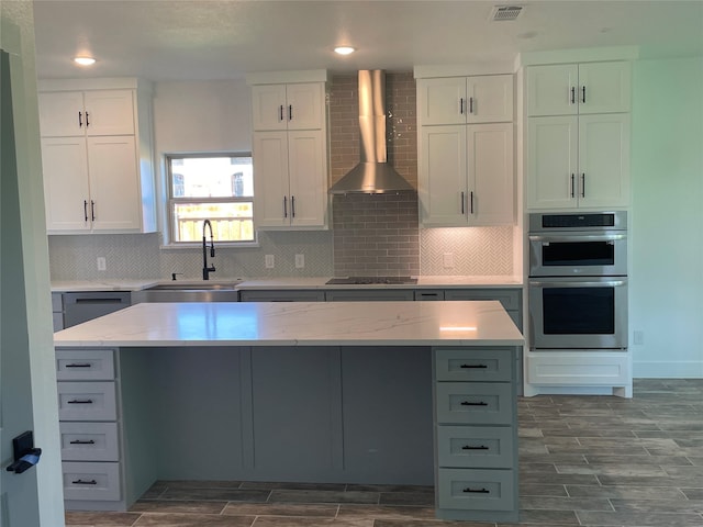 kitchen featuring wall chimney exhaust hood, stainless steel double oven, a center island, and sink