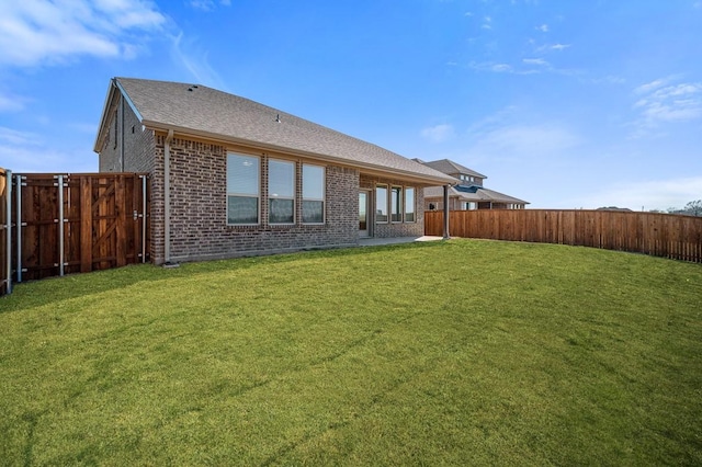 back of property featuring a yard, a fenced backyard, roof with shingles, and brick siding