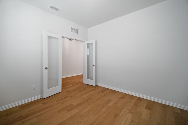 empty room with light wood finished floors, baseboards, visible vents, and french doors