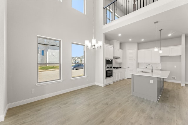 kitchen with sink, a high ceiling, an island with sink, white cabinets, and light wood-type flooring