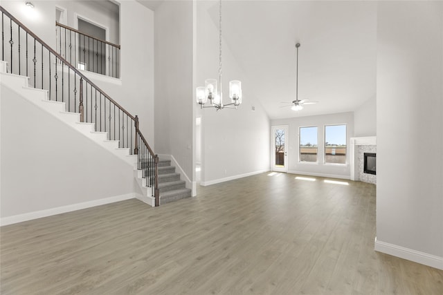 unfurnished living room with hardwood / wood-style floors, a high ceiling, and ceiling fan with notable chandelier