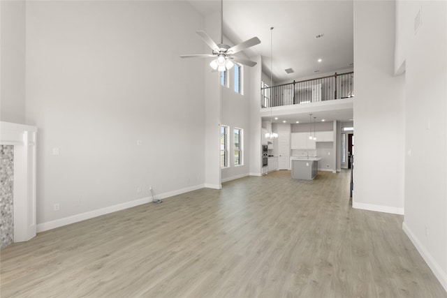 unfurnished living room with ceiling fan, a towering ceiling, and light hardwood / wood-style floors