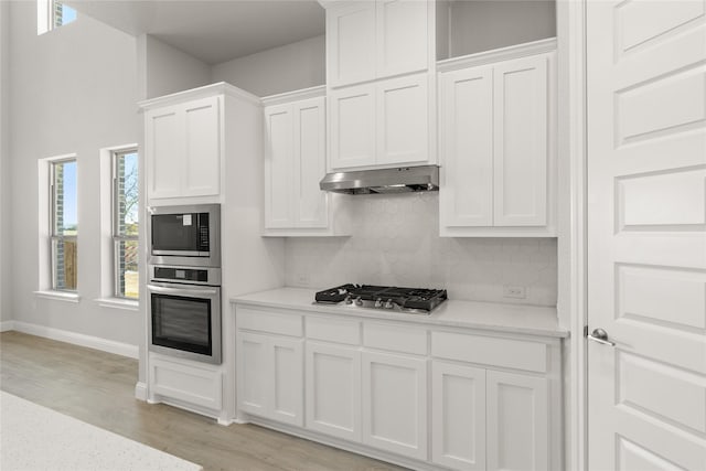 kitchen featuring white cabinets, decorative backsplash, light wood-type flooring, and appliances with stainless steel finishes