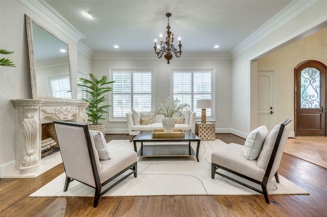 sitting room featuring a fireplace, light wood-type flooring, crown molding, and an inviting chandelier