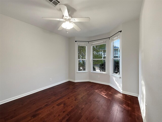 empty room featuring dark wood-style floors, baseboards, a ceiling fan, and visible vents