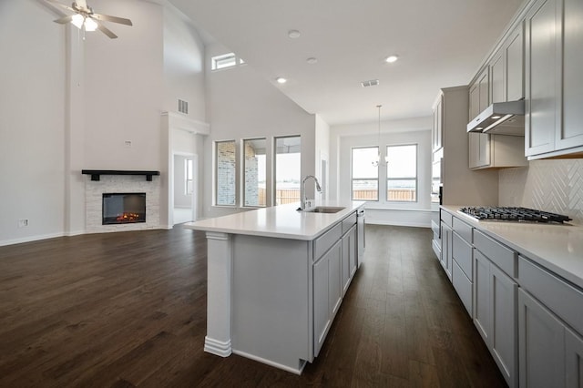 kitchen featuring stainless steel gas stovetop, gray cabinetry, dark wood-type flooring, a sink, and under cabinet range hood