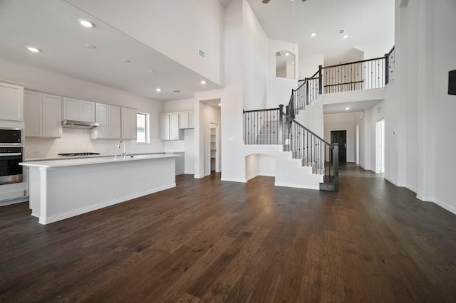 kitchen featuring under cabinet range hood, dark wood-style flooring, light countertops, appliances with stainless steel finishes, and a center island with sink