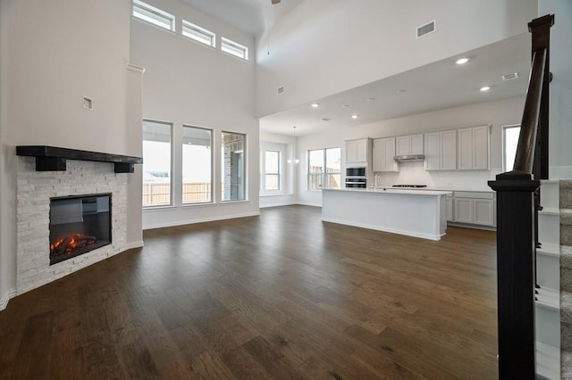 unfurnished living room featuring dark wood-type flooring, a fireplace, a sink, visible vents, and stairs