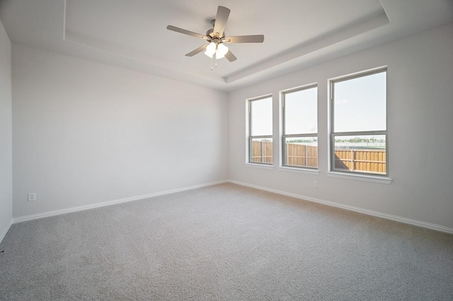 spare room with carpet floors, a raised ceiling, a ceiling fan, and baseboards