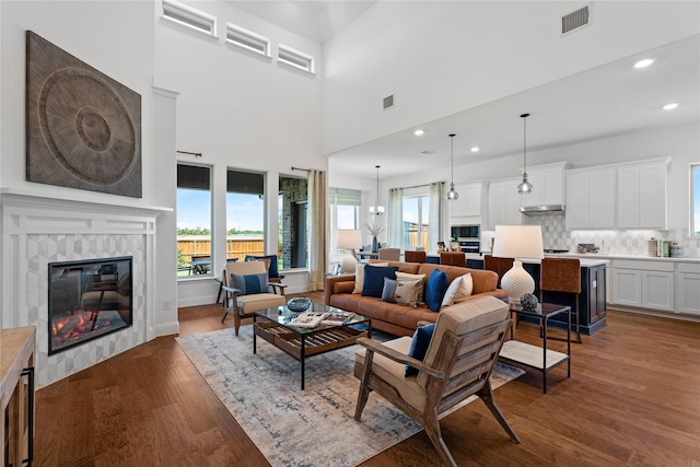 living room featuring wood-type flooring, a tiled fireplace, and a towering ceiling