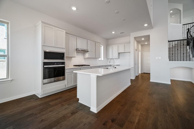 kitchen with dark wood-style flooring, light countertops, appliances with stainless steel finishes, a sink, and under cabinet range hood