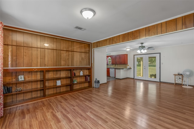 unfurnished living room featuring ceiling fan, french doors, light hardwood / wood-style floors, ornamental molding, and wood walls