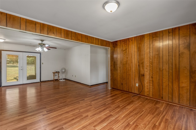 empty room with french doors, wooden walls, and light wood-type flooring