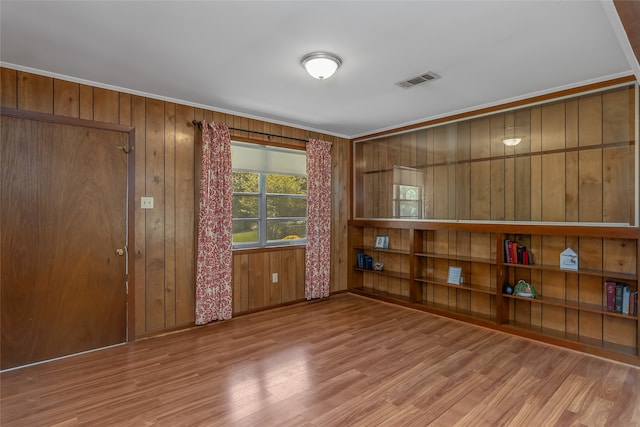 empty room with wood walls, crown molding, and light hardwood / wood-style flooring