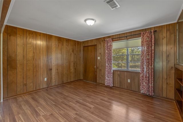 spare room with ornamental molding, wooden walls, and hardwood / wood-style floors