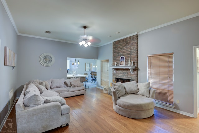 living room with light wood-type flooring, a brick fireplace, a high ceiling, ceiling fan with notable chandelier, and crown molding