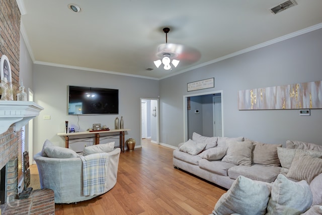 living room featuring a brick fireplace, light wood-type flooring, ornamental molding, and ceiling fan