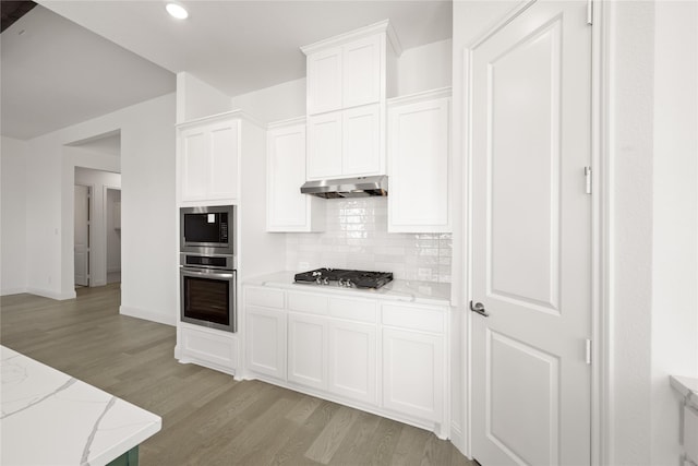 kitchen with light stone counters, light hardwood / wood-style flooring, white cabinets, and appliances with stainless steel finishes