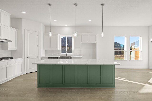 kitchen with white cabinets, pendant lighting, a center island, and light stone countertops