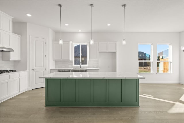 kitchen featuring light stone countertops, a center island, white cabinets, and decorative light fixtures