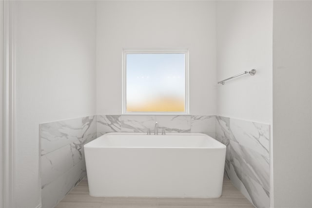 bathroom with a tub to relax in and tile walls