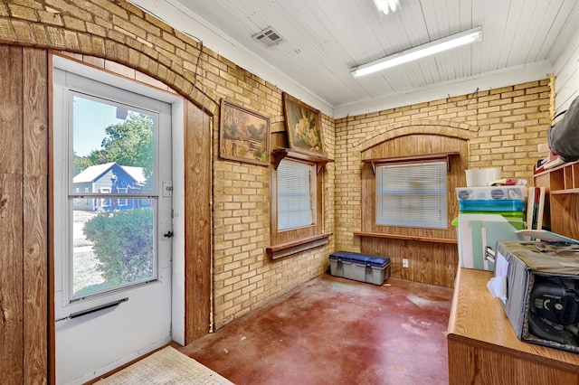 entryway with crown molding, wood walls, brick wall, and concrete floors