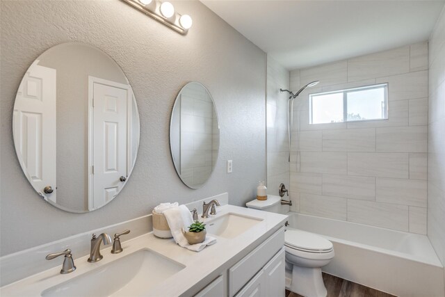 full bathroom featuring hardwood / wood-style floors, vanity, tiled shower / bath combo, and toilet